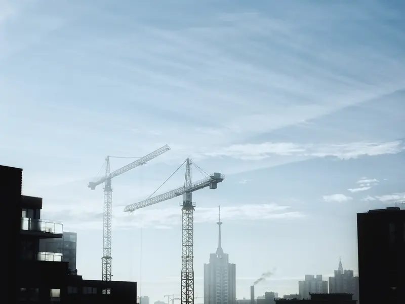Construction cranes silhouetted against a city skyline at dawn